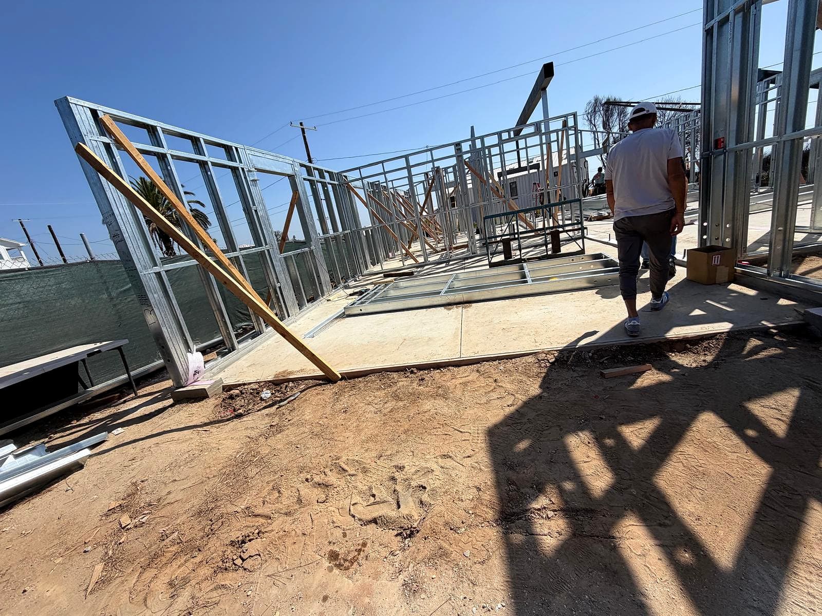 Exterior walls stood up along the slab and held plumb with temporary wood braces. A long line of steel-framed exterior walls on a concrete slab, held plumb by diagonal wood braces